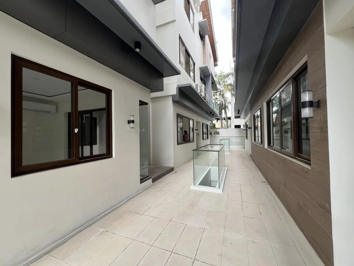 The same ground-level covered walkway from a slightly different angle, showing the tiled floor, glass skylight panels, and the brown accent wall with windows on the right